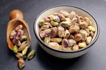 Peeled pistachio nuts in a bowl over black background. Baked pistachios pile, salt pistache, salted pista. Copyspace