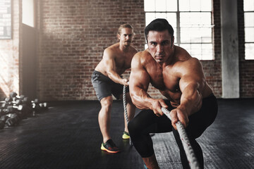 This is what fit and fierce looks like. Shot of two muscular young men pulling on a rope in a gym.