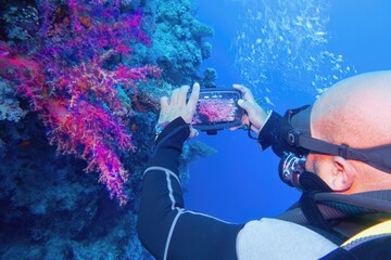 Man scuba diver using smartphone underwater housing when shooting coral reef scenery. Modern...
