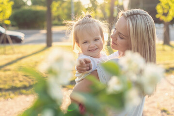 Mom and child outdoor. Happy mother and little daughter in the park on a sunny day at sunset.  Concept of tenderness, family single mother, flowers, smiles, hugs, mental health, harmony, peace