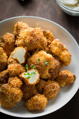 crispy breaded cauliflower with herbs and sauce in a white plate on a brown background vertical photo