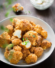 crispy breaded cauliflower with herbs and sauce in a white plate on a brown background vertical photo