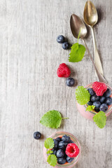 Fresh homemade yogurt in a glass jar with blueberries, raspberries, mint and Passionfruit. Metal vintage spoon. Light wood background. Top view