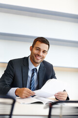 Obraz premium Making sure his documents are in order. A handsome young businessman sitting at his desk and reading through some paperwork.