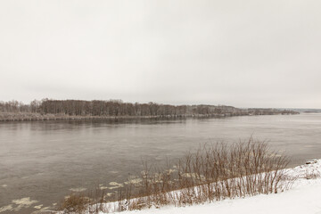 Fototapeta premium A river in spring or winter with unfrozen water. There are trees in the snow on the shore.