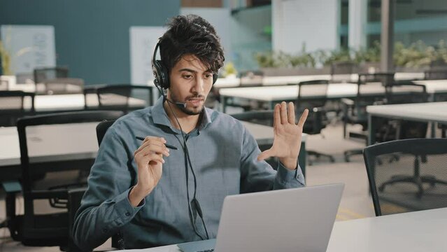 Young Indian businessman investor wearing headphones communicate by video call conference on laptop negotiation talk online with employee distant consulting clients virtual training concept in office