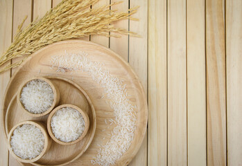 Jasmine rice in a bowl on dark wooden table with rice plants, ear of rices with jasmine rice in a...