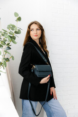 Portrait of a young blonde girl in a jacket and jeans, holding a handbag. fashionable women's leather clutch bag. Traditional women's clutch bag with gold hardware. Fine coloured leather handbag. 