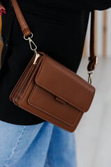 Girl holding her handbag, close-up. Small fashionable women's leather clutch bag with fabric strap in shoe tone. Girl's Traditional clutch bag with brooch. handbag made of fine coloured genuine leathe