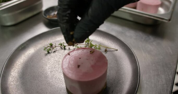 hands add decorations to a small round pink dessert from the restaurant kitchen to serve fresh vegan cuisine, rav dessert vegetriano, natural, vegetable food, plants, macro close-up shot