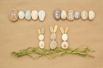 Happy Easter lettering and bunnies from pebbles on craft paper background. Ecological zero waste, eco friendly nature concept. Flatlay, lay out, top view.