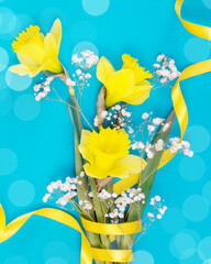 Holiday flower composition with bouquet of yellow daffodils with gold ribbon on blue background. Flower card suitable for Womens Day, 8 March or Mothers Day