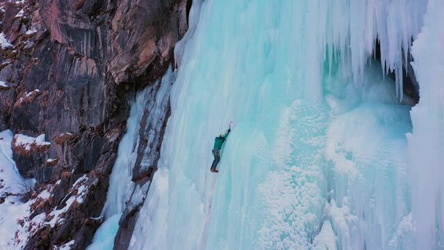 Ice Climbing on Frozen Waterfall, Aerial View. Barskoon Valley, Kyrgyzstan. Drone Flies Upwards, Tilt Down. Crane Shot