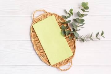 Green kitchen tea towel and eucalyptus branch on a wicker tray on a white wood table