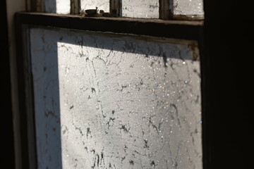 Old fashion window covered in frost with morning light shining thru the glass, dark contrast inside, shadows and light.