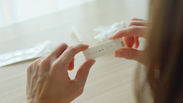 Self test of Coronavirus infected patient using ATK rapid test kit to check the positive result at home. Close up shot of woman holding antigen test kit with stress feeling to know the 2 stripe result
