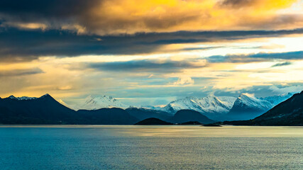 Vom Sonnenaufgang orange gefärbte Wolken über den frisch verschneiten Bergen der Küste von Norwegen, zwischen Nesna und Ørnes im Nordland. 