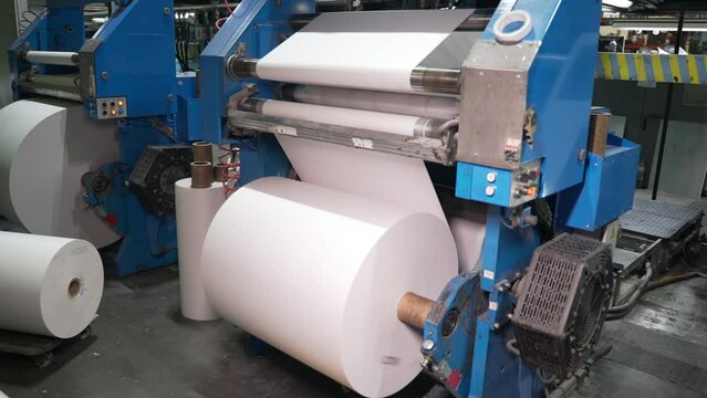 Paper for printing newspapers and magazines. Large bobbin with a roll of white paper is spinning on the machine. Printing house, publishing house. Media, print edition, journalism, politics