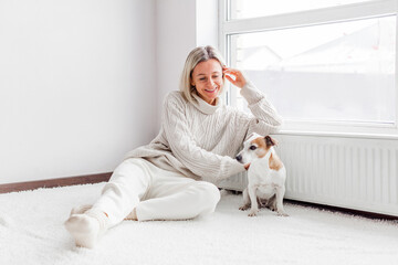 serene adult woman with dog near radiator in the living room at home - obrazy, fototapety, plakaty