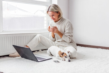 Happy middle aged woman with dog using her laptop at cozy white home