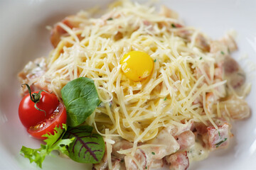 Pasta with bacon, white sauce and fresh quail egg. Served on a white plate with red tomatoes.