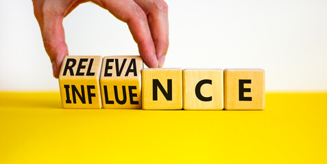 Influence or relevance symbol. Businessman turns wooden cubes and changes the word Influence to Relevance. Beautiful yellow table white background. Business influence or relevance concept. Copy space. - obrazy, fototapety, plakaty