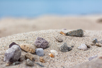 Fototapeta na wymiar Sand mountain on the beach full of stones, blurry sea, and sand background. a pile of nice beach sand with and stones