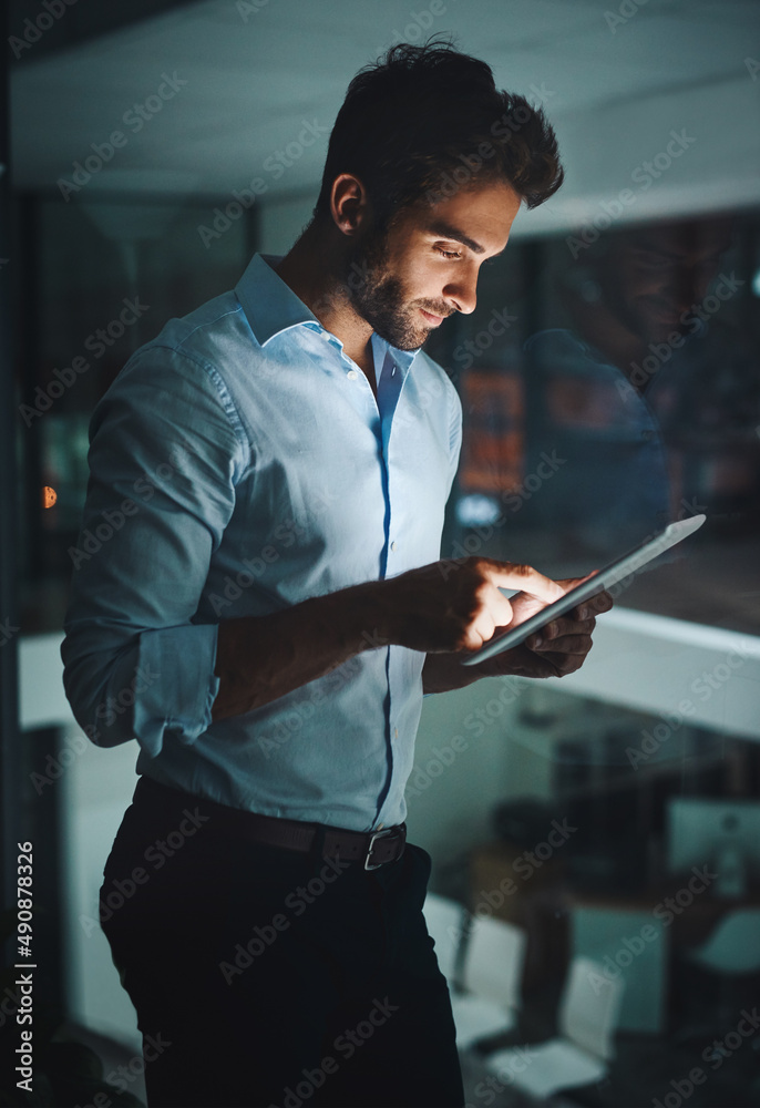 Poster the tool to keep you connected 247. shot of a young businessman working late on a digital tablet in 