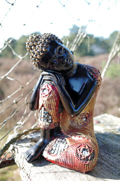 Dreamy decorative Buddha sits on a bench outside.