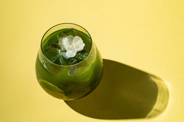 Ice matcha lemonade in transparent glass, bright yellow background, harsh studio light, copy space