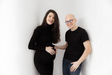 Pregnant brunette girl in a black dress with a throat and a man in a T-shirt and jeans on a gray background