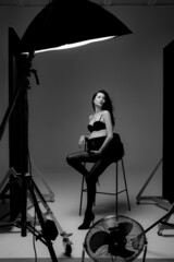 Pregnant brunette girl in pantyhose, bra and shoes on a high chair in a photo studio