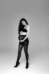Pregnant brunette girl in pantyhose, bra and shoes in a photo studio