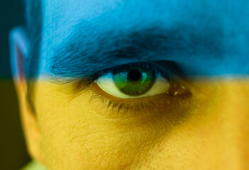 Naklejka premium Close up of an angry male green eye. Blue and yellow colors on his face as symbol of patriotism and inviolability of Ukraine
