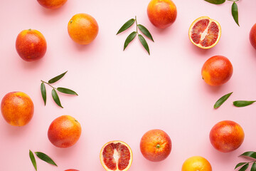 Blood oranges sliced and whole with sprigs of green leaves on a pink background, space for text. Top view.