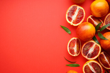 Blood oranges sliced and whole with sprigs of green leaves on a red background, space for tex, top view.