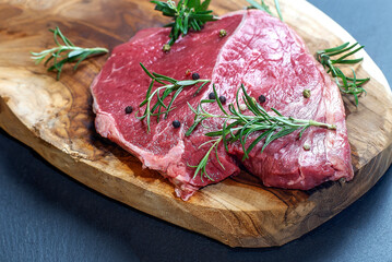 Raw rib-eye steak on wooden Board on grey background with salt, pepper and rosmary in a rustic style