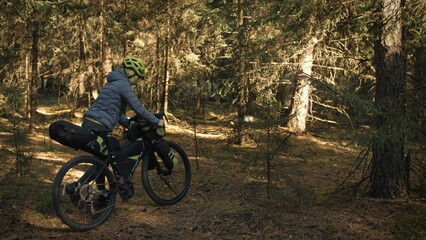 Fototapeta premium The woman travel on mixed terrain cycle touring with bike bikepacking outdoor. The traveler journey with bicycle bags. Stylish bikepacking, bike, sportswear in green black colors. Magic forest park.