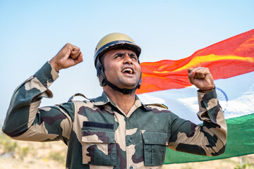 excited army service man shouting by looking above in front of waving indian flag - concept of...