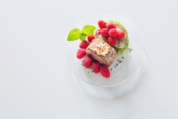 chocolate roll with raspberries and mint leaves on glass plate on  white table