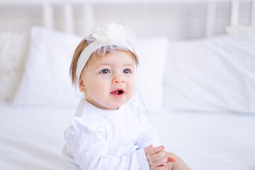 a large portrait of a cute and joyful baby girl in a crib in white clothes, a funny little child at home, the concept of children's goods