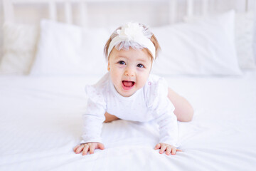 cute baby girl sitting on the bed in white clothes and with a bow on her head and crying, funny...