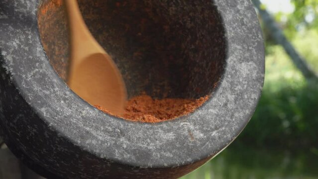 Small bamboo spoon is taking a mix of spices and peppers from grey stone mortar