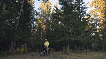 Naklejka premium The man travel on mixed terrain cycle touring with bike bikepacking outdoor. The traveler journey with bicycle bags. Stylish bikepacking, bike, sportswear in green black colors. Magic forest park.