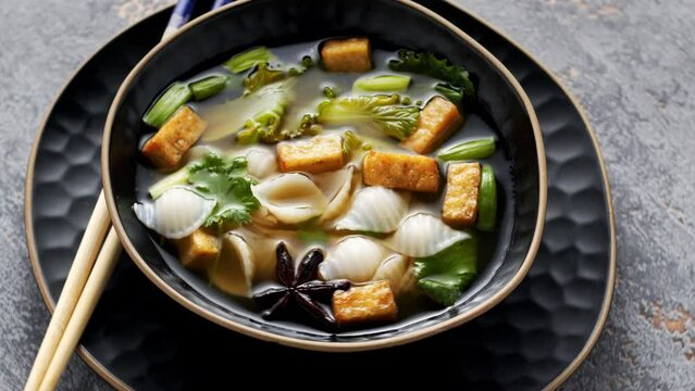 Pho soup with fried tofu cubes, noodles, pak choi and vegetables. Table spin, zoom-in.