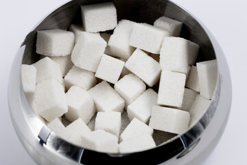 a lot of cubes of white refined sugar for tea and coffee in a metal sugar bowl with nirror reflections top view close-up