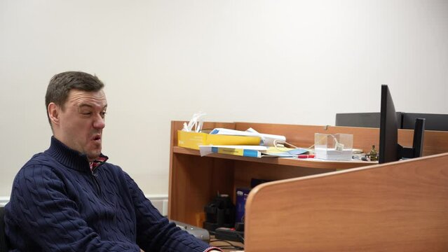 Millennial man looking disgusted in front of his computer in office. Confused businessman in blue sweater cringe and looking at screen with squeamishness at startup business office space