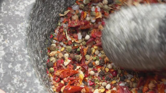 Close-up of a pestle grinding and mixing various spices, peppers and sea salt