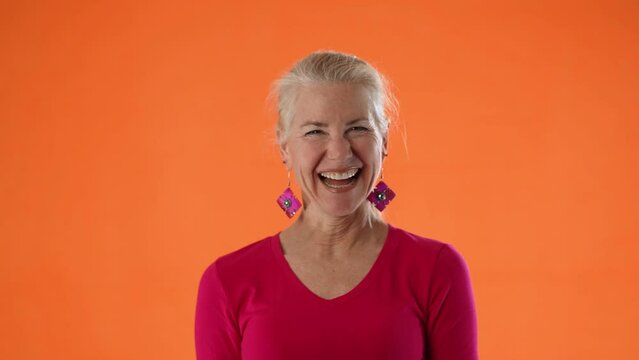 Portrait of mature woman happy laughing at camera isolated on orange background copy space.