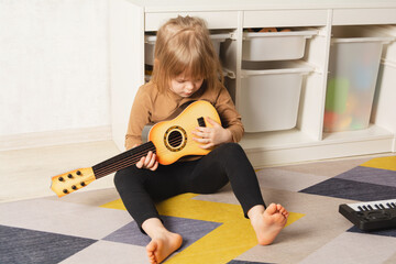 Child at home learning to play the guitar. Leisure and education at home. Child portrait looking to...